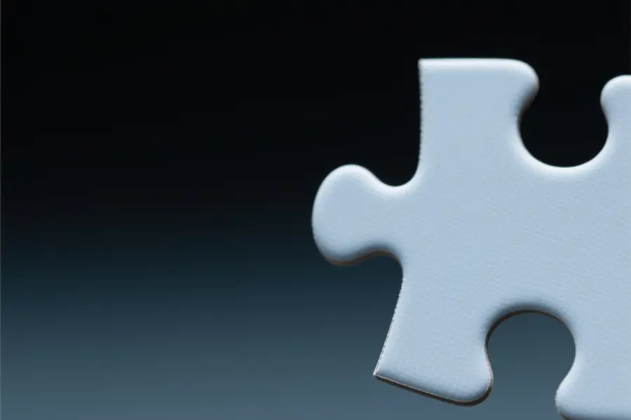 Close up of a slate colored puzzle piece floating in a gradient space